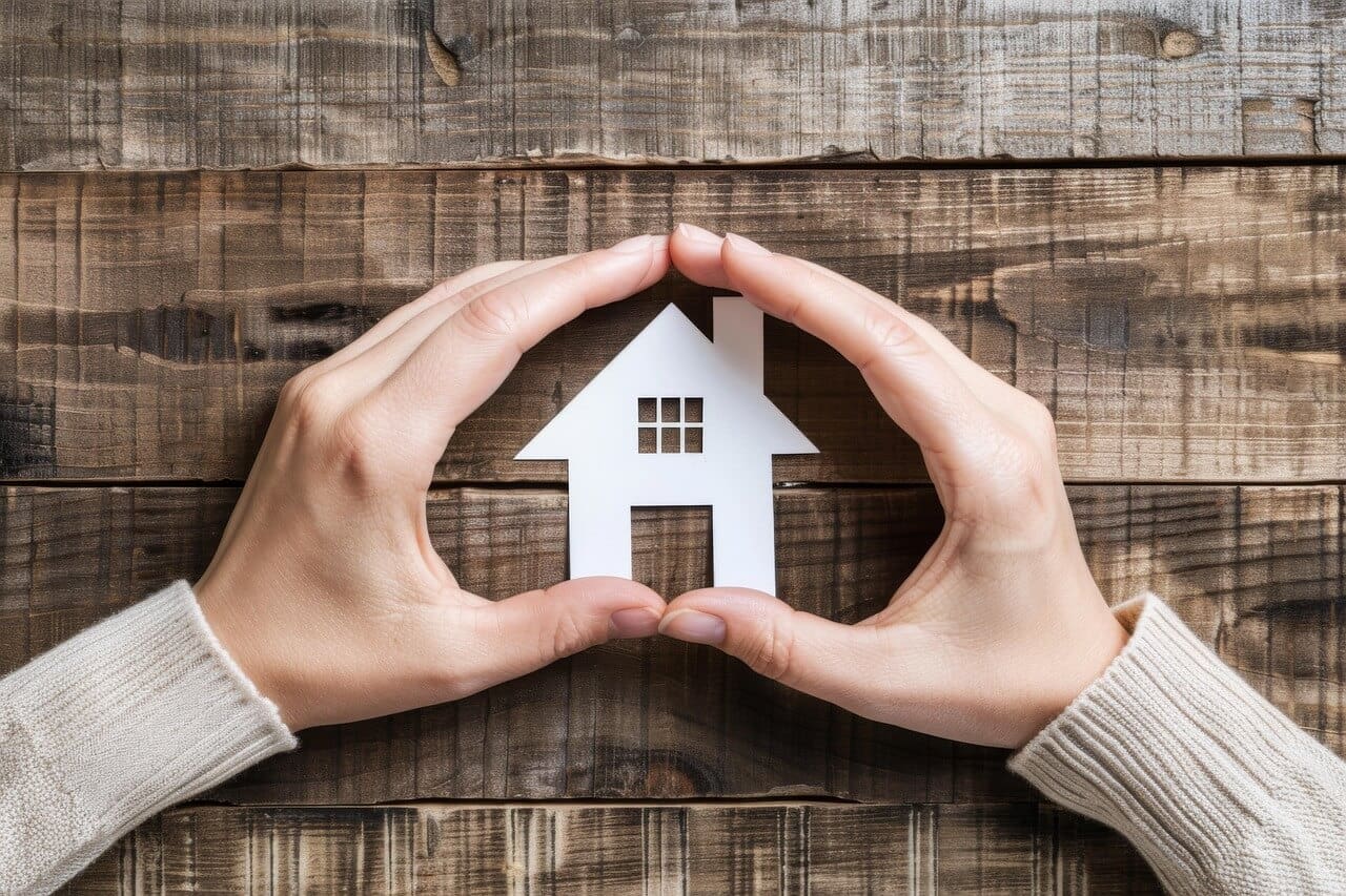 Hand holding a heart-shaped symbol with a house, representing home insurance protection and security.
