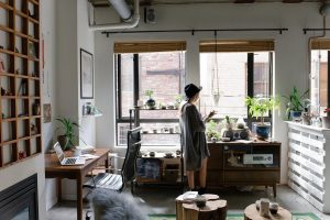 A woman standing in a room with a window of her house thinking about her home insurance.